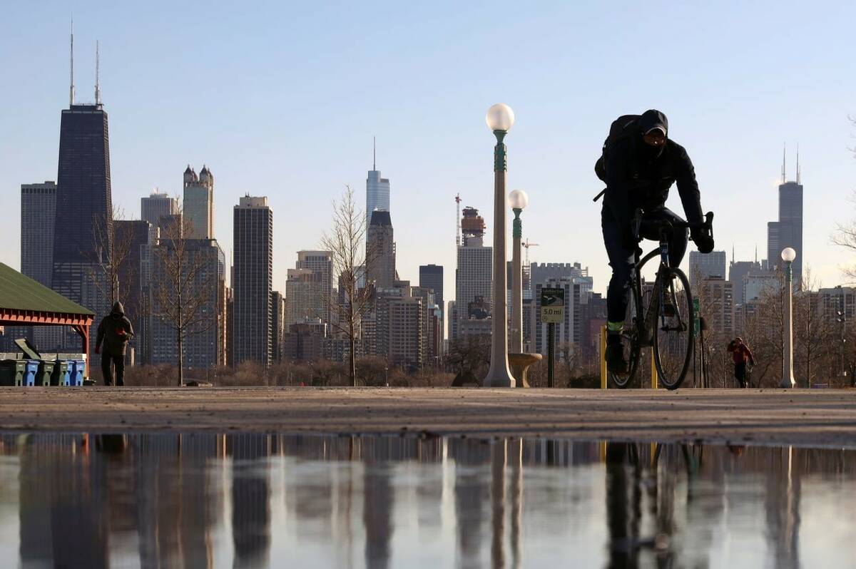 Chicagos skyline reflekteras i vattnet i den tinade snön när en cyklist passerar vid Nort ...